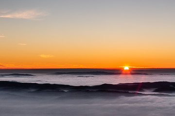 Obraz premium Beautiful sunset over a valley filled by fog with mountains and hills