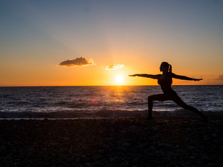 Naklejka na ściany i meble Silhouette woman practicing yoga or stretching on the beach pier at sunset or sunrise. Yoga practice, meditation and healt concept.