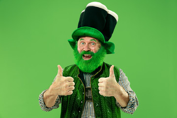 A smiling surprised happy senior man in a leprechaun hat with beard at green studio. He celebrates...