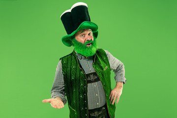 A smiling surprised happy senior man in a leprechaun hat with beard at green studio. He celebrates...