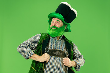 A smiling surprised happy senior man in a leprechaun hat with beard at green studio. He celebrates...