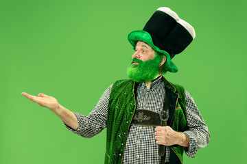 A smiling surprised happy senior man in a leprechaun hat with beard at green studio. He celebrates...