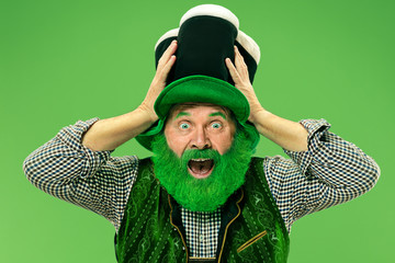 A smiling surprised happy senior man in a leprechaun hat with beard at green studio. He celebrates...