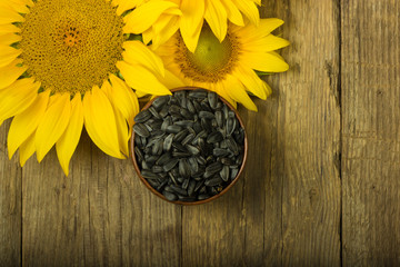 seeds of sunflower in wooden cup  and heap of sunflowers on wooden background