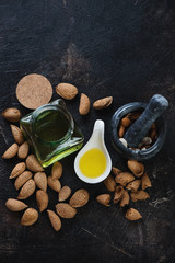 Freshly made almond oil, unpeeled almond nuts and a marble pounder. High angle view on a dark brown stone background with copyspace