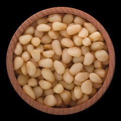 peeled cedar nuts in wooden cup isolated on black background. top view