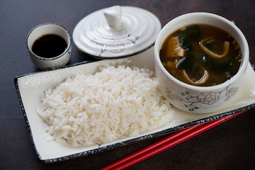 Plate with white rice and a bowl of miso soup, studio shot on a dark brown metal surface