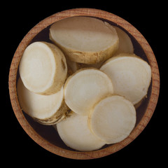 slices of horseradish in wooden cup isolated on black background. top view