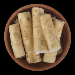 slices of horseradish in wooden cup isolated on black background. top view