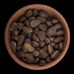 cedar nuts in wooden cup isolated on black background. top view