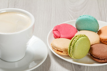 Cup of coffee and delicious macarons cakes of different color on plate