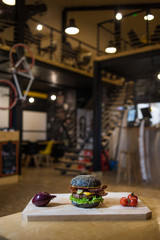 An appetizing black hamburger on a wooden board with fresh vegetables.