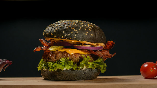 An appetizing black hamburger on a wooden board with fresh vegetables.