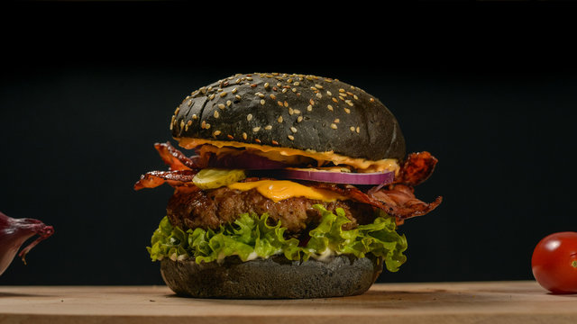 An appetizing black hamburger on a wooden board with fresh vegetables.