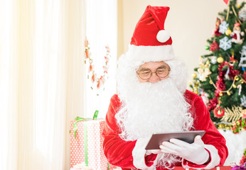 Closed up of hands Senior Santa Claus with tablet pc at home .Happiness Santa Claus has a gift box for children .Christmas, holidays, new year, technology and shopping concept