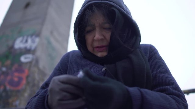 Portrait adult homeless woman with plaid sits on the bridge in cold windy grey weather crying and taking pills