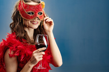 Smiling mystery woman in a red carnival mask and boa with a raised glass of wine. - Image