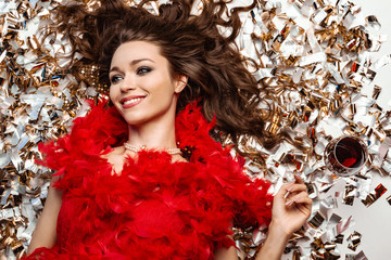 Happy young woman lying on the floor among golden tinsel, smiling close-up next to a glass of red wine