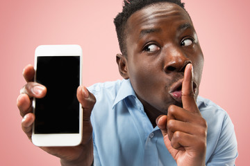 Indoor portrait of attractive young black african man isolated on pink background, holding blank smartphone, showing screen, feeling scared, wary and surprised. Human emotions, facial expression