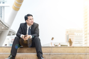 Manager professional businessman sitting on the steps stairs in city .Young asian man wear glasses in formal clothes  looking to the side ,with copy space