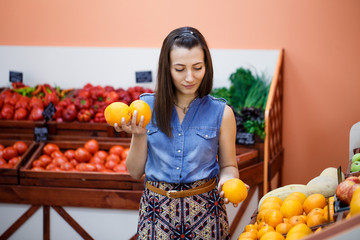 Young woman chooses oranges in a vegetable store