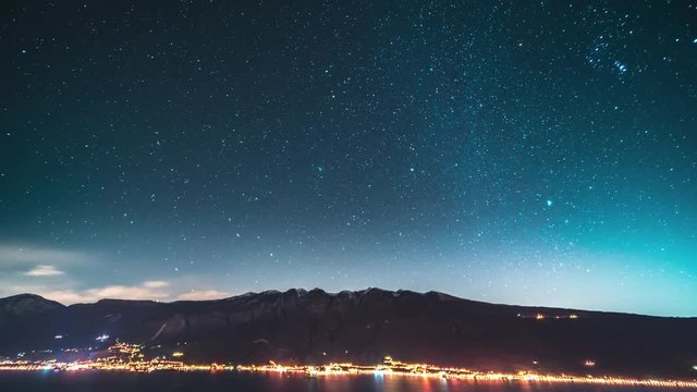 Timelapse of moving star trails in night sky over the mountain range and Garda lake on a foreground, Italy