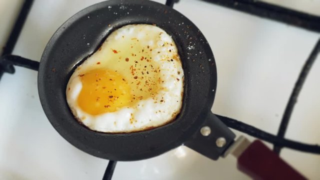 Cooking a fried egg with seasoning on a mini pan in the shape of a heart for Valentine's Day. Slow motion shot