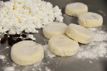 Raw cheese cakes with flour and cottage cheese on a metal table