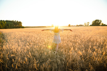 Young female standing in the field with hands spread towards the sun enjoying life