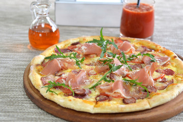 Delicious pizza with prosciutto, sausages and tomatoes, with spicy sauce and tomato juice on a wooden plate 