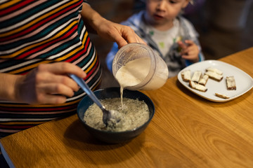 Fototapeta na wymiar Mother preparing oatmeal breakfast to infant son at the kitchen.