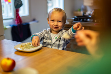 Father trying to give breakfast to infant son during the morning at the kitchen.