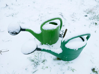 two green watering cans side by side covered in snow