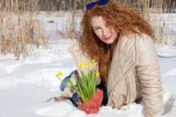 Pleasant fashionable curly haired woman sitting in snow with yellow narcissus