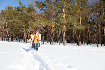 Naklejka premium Horizontal photo of red haired woman walking through snowdrifts with yellow narcissus in hand