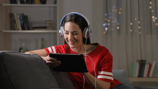 Happy teen watching and listening media on tablet sitting on a couch in the night at home