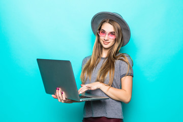 Portrait of young smiling woman in hat holding laptop on blue background