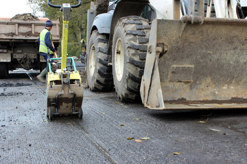 A road construction worker compacts the soil with a compact vibroplate before asphalting a problematic swampy section of the road. Russia, entry in the city of Gatchina. Reportage.