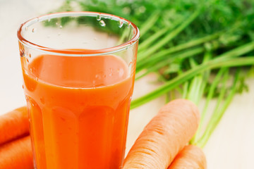 Fresh carrot juice in glass on wooden table background.