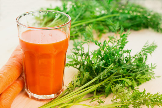 Fresh carrot juice in glass on wooden table background.