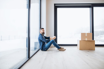 Fototapeta premium A mature man with cardboard boxes sitting on the floor, furnishing new house.