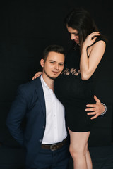 pregnant couple hugging on black background. Lovers fashionable young man and woman