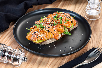Close up view on sandwich with salmon, microgreen and avocado on a black plate. Healthy food for menu. Free copy space. Healthy diet background