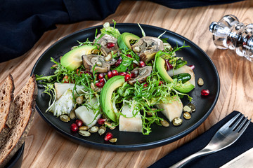 Healthy green vegetarian salad bowl lunch with avocado, artichokes, pomegranate seeds on dark plate. Food dish on wooden background. Healthy food for menu. Free copy space. Healthy diet background