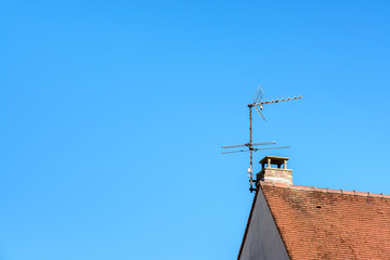 Fototapeta na wymiar Low angle view of a TV antenna fixed to the chimney on the tile roof of a detached house against blue sky.