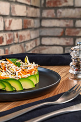 Green vegetarian salad lunch with avocado, carrot and cabbage on dark plate. Close up food dish on wooden background. Food and health for menu. Free copy space. Healthy diet background.