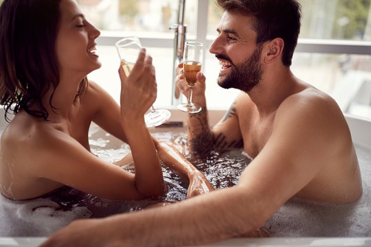 Attractive man and woman enjoying and relaxing in the bathtub and drinking champagne .