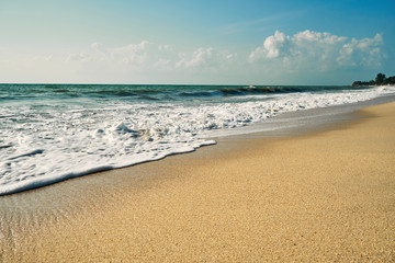 Wild sandy beach with surf. Blue sky in the background