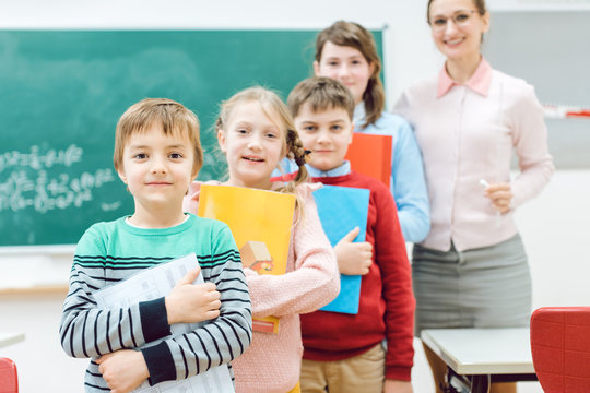 Sch&uuml;ler mit B&uuml;chern und die Lehrerin stehen im Klassenzimmer 