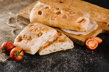Fresh baked bread with tomatoes on black wooden background